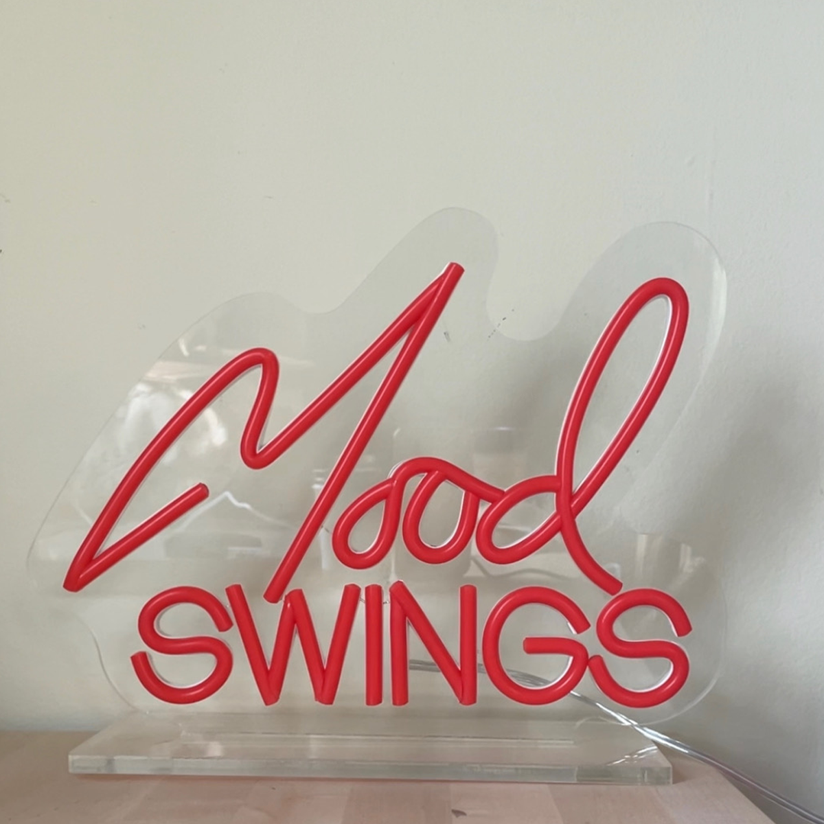 Red neon-style sign reading ’Mood SWINGS’ mounted on a clear acrylic base.