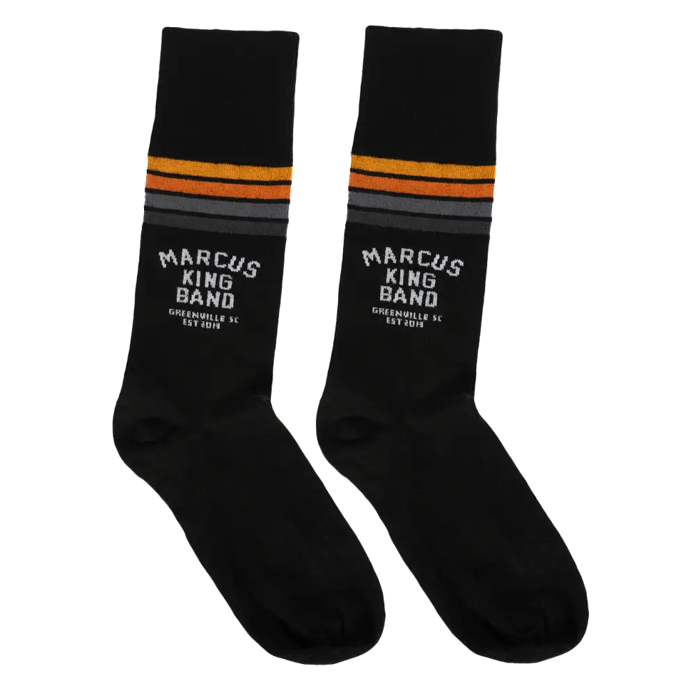 Black socks with orange and gray stripes near the top, featuring white ’marcus king band’ text and ’greensville sc est 2019’’ below.