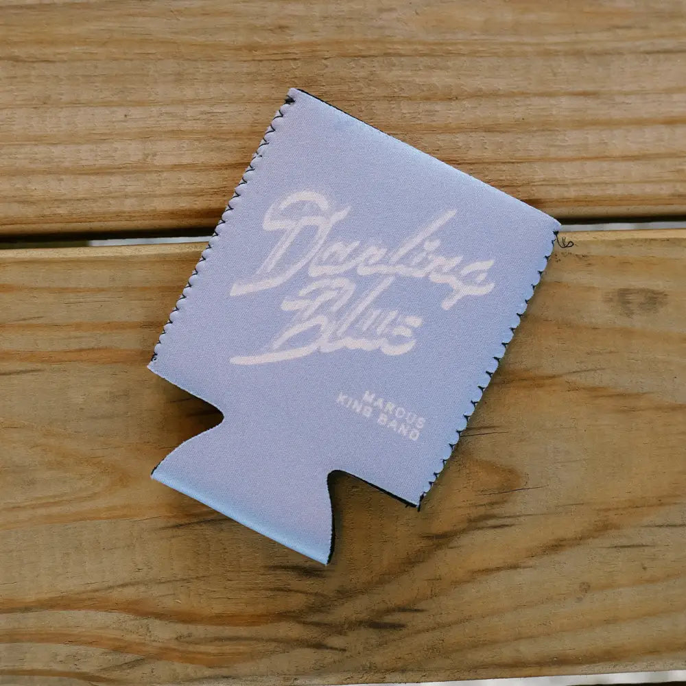 Light blue fabric koozie with white cursive ’dueling blues’ and smaller text below reading ’marcus king band.’